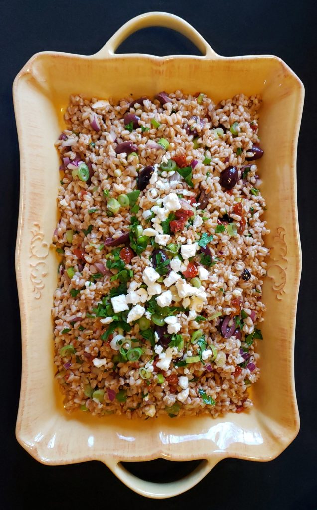 A family style platter of Healthy Mediterranean Farro Salad is ready to be served. Farro, kalamata olives, sun dried tomatoes, fresh scallions, red onions and feta cheese are tossed with a light lemon and olive oil vinaigrette.