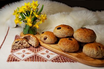 Stacked on top of a rustic wooden cutting board, sits a neat stack of Easy Nordic Rye Rolls in 3 Hours. The board rests upon a faux polar bear fur and nordic print linens. Vibrant spring flowers give the appearance of warmer weather breaking.