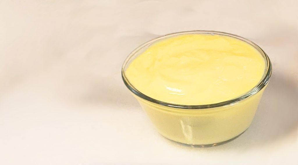 A silky serving of Delicious Classic Vailla Pastry Cream in 10 Min. sits in a cool glass ramekin atop a marble board. Simple and oh, so delicious!