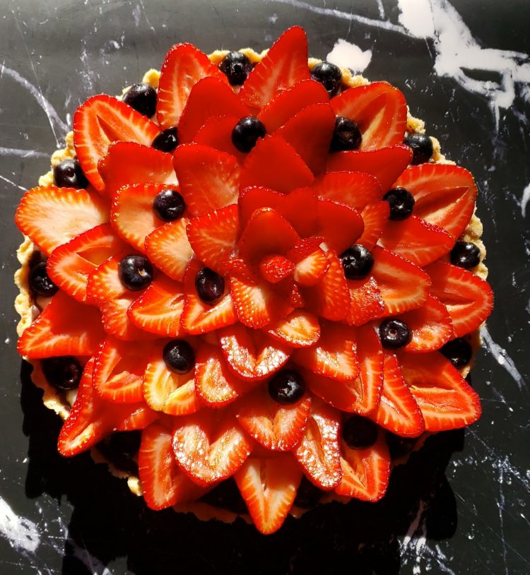 A closeup shot of this Beautiful 3 Step Seasonal Fresh Fruit Tart. A flaky shell is brushed with dark chocolate, then filled with a silky vanilla pastry cream and topped with fresh seasonal fruit. Strawberries adorn the top of the tart.