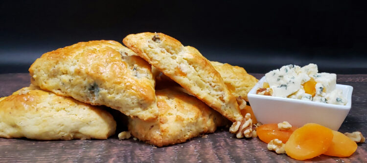 A plate of Perfect Gorgonzola Apricot and Walnut Scones is surrounded by dried apricots, gorgonzola crumbles and walnuts.