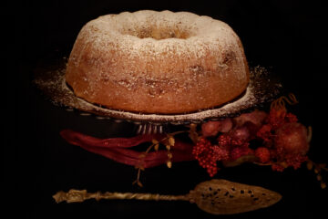 A Delicious 5-Layer Romanian Coffee Cake is dusted with white powdered sugar and sits majectically upon an elegant, glass cake stand. Holiday decorations provide a festive backdrop.