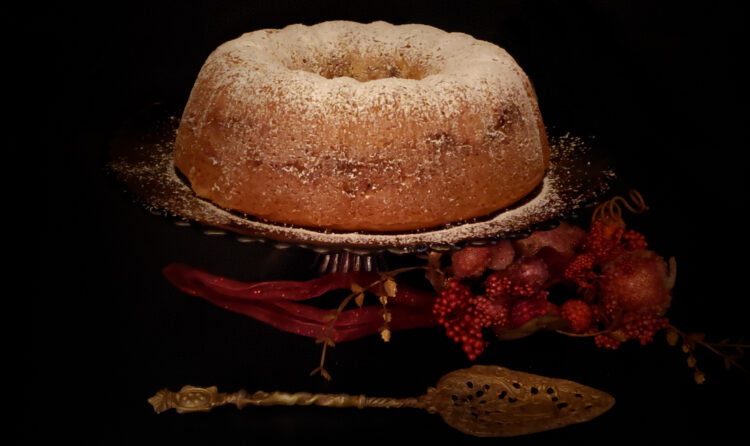 A Delicious 5-Layer Romanian Coffee Cake is dusted with white powdered sugar and sits majectically upon an elegant, glass cake stand. Holiday decorations provide a festive backdrop.