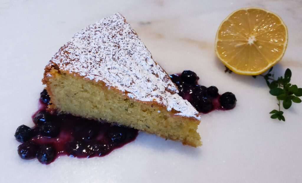 A slice of Gluten Free Lemon Thyme Cornmeal Cake is topped with fresh blueberry sauce.