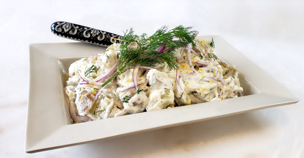 A generous bowl of Ultimate Lemon Dill Potato Salad is topped with fresh dill and lemon zest.