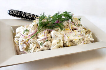 A generous bowl of Ultimate Lemon Dill Potato Salad is topped with fresh dill and lemon zest.