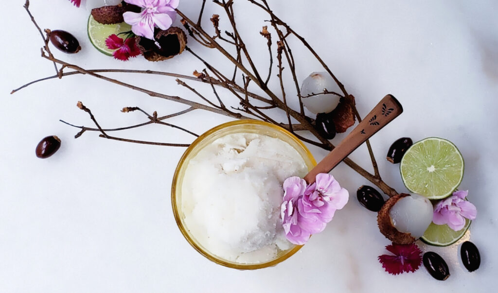 Easy 4-Ingredient Lychee Coconut Sorbet. A frosty bowl of lychee coconut sorbet sits nestled among lychee twigs, peeled lychee fruit, lime slices and fresh flowers.