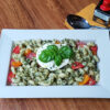 A beautiful platter of Delicious Caprese Pesto Pasta Salad is topped with fresh mozzarella cheese, basil and vine ripe tomatoes.
