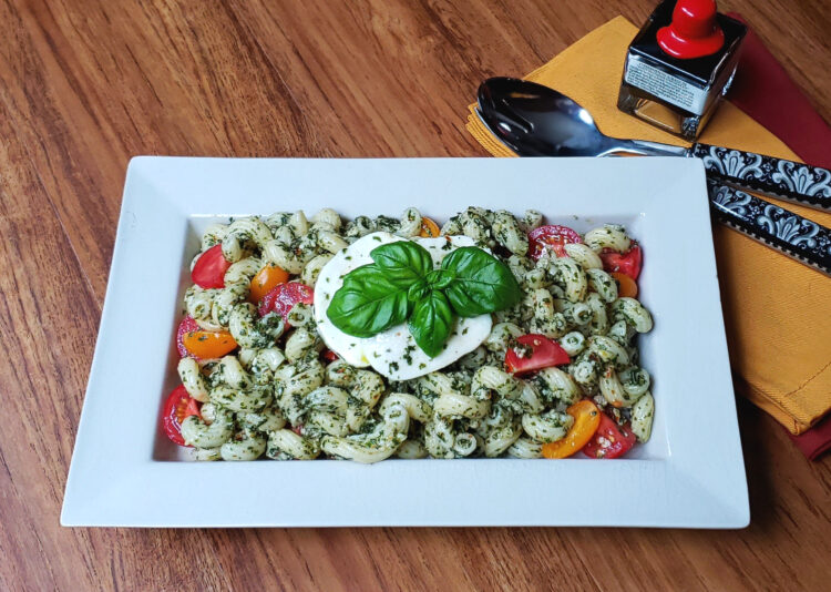 A beautiful platter of Delicious Caprese Pesto Pasta Salad is topped with fresh mozzarella cheese, basil and vine ripe tomatoes.