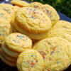 A large stand plate of Easy Mascarpone Orange Drop Cookies in 10 Minutes are nestled among flowers in a garden.