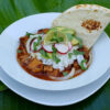 Easy Slow Roasted Pork Pibil. Vibrant green banana leaves serve as the place mat for this beautiful, fresh dish. Fork-tender pork in its own sauce is topped with white rice, thinly-sliced onions, radishes, fresh cilantro, avocado and a lime wedge. A pan-toasted tortilla is nestled next to the pork.