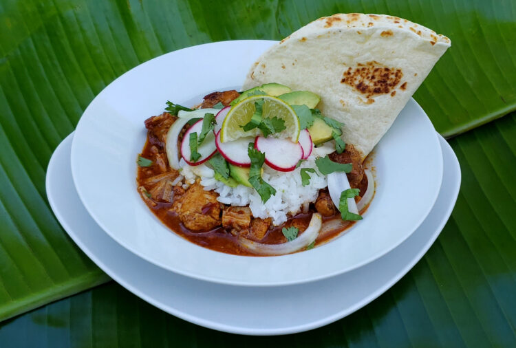 Easy Slow Roasted Pork Pibil. Vibrant green banana leaves serve as the place mat for this beautiful, fresh dish. Fork-tender pork in its own sauce is topped with white rice, thinly-sliced onions, radishes, fresh cilantro, avocado and a lime wedge. A pan-toasted tortilla is nestled next to the pork.