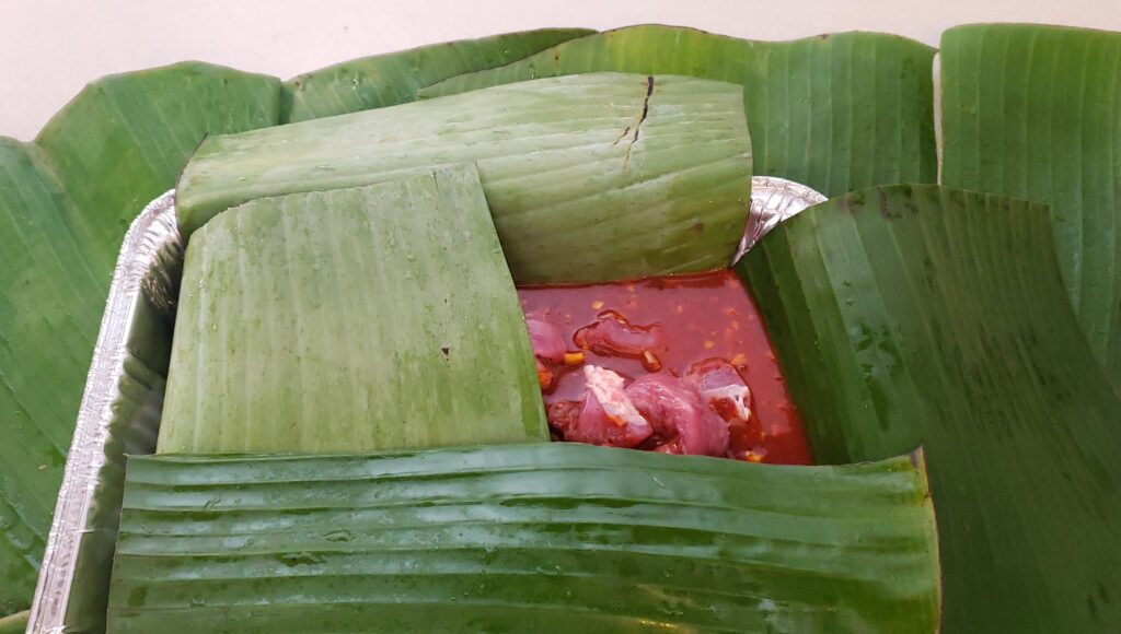 Image shows the process of wrapping the pork in banana leaves before roasting in the oven.