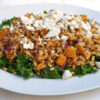 A large oval, family-style platter displays a generous portion of this Easy Butternut Squash Farro Salad with 5-Ingredient Dressing. A bed of fresh, crisp kale frames the salad. Butternut squash, red onion, fresh parsley and feta crumbles invite you to dive in.