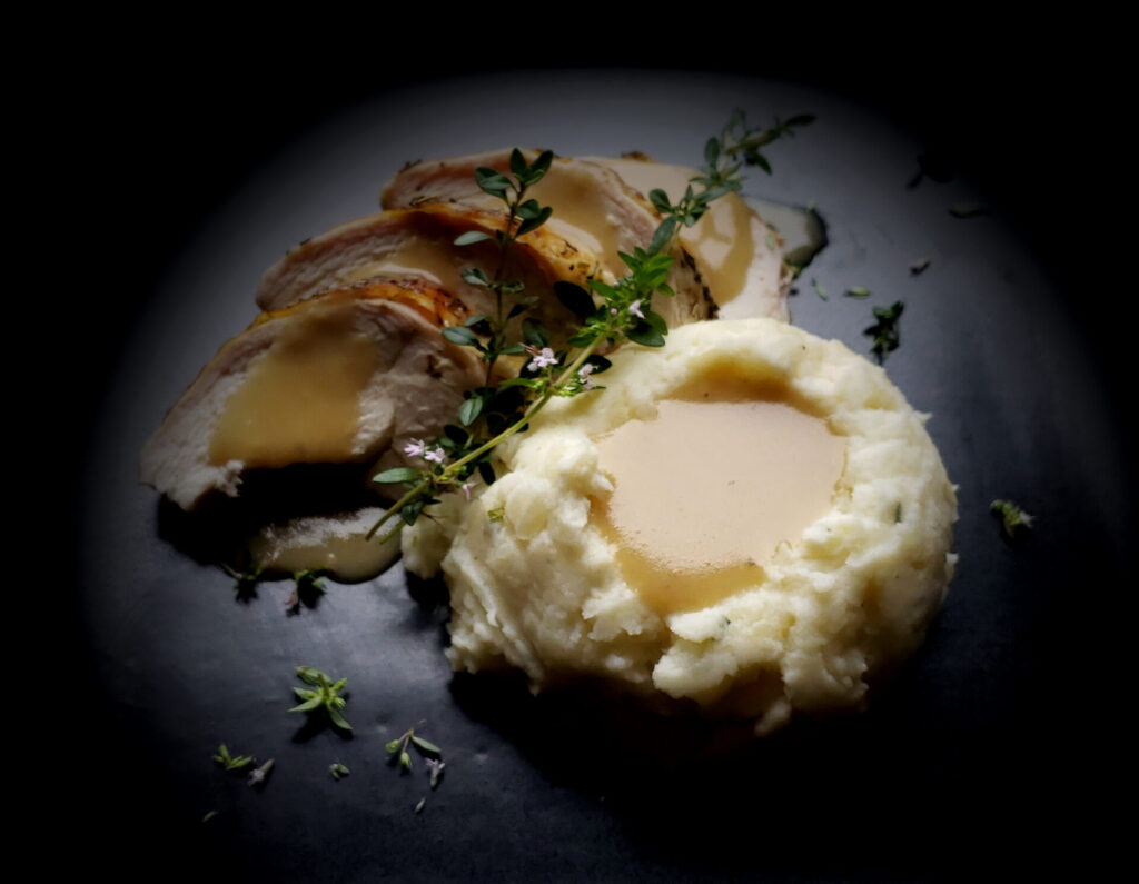 Perfect Chive and Horseradish Mashed Potatoes. Slices of herb crusted roast chicken, generously drizzled with gravy provide the background for these perfectly seasoned mashed potatoes. In the center of the potatoes is a generous portion of gravy - nearly ready to spill over the edge onto the plate.