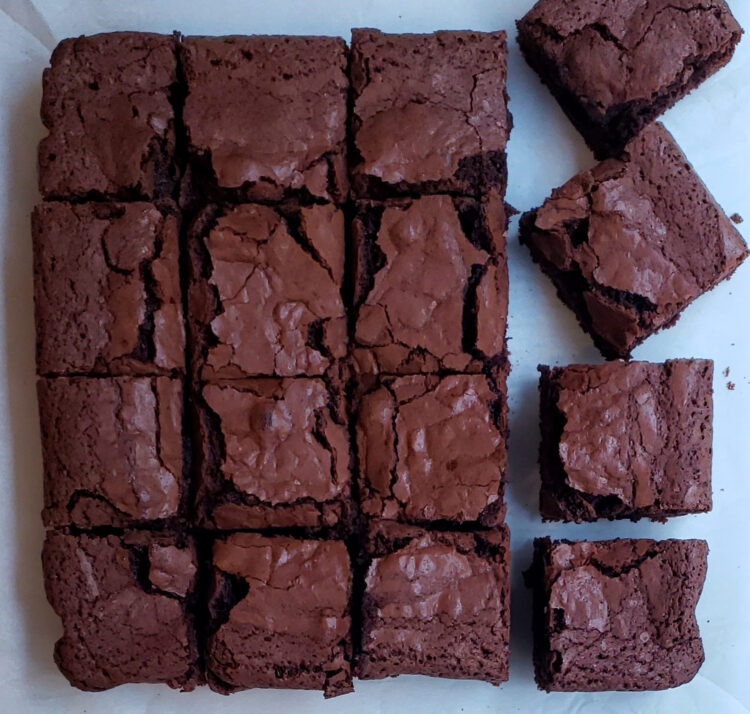 GF Brown Butter Brownies. A freshly baked pan of gluten free brown butter brownies have been neatly cut into 16 perfect squares. The last row on the right is slightly jumbled - giving it the appearance that someone is stealing a still-warm square.