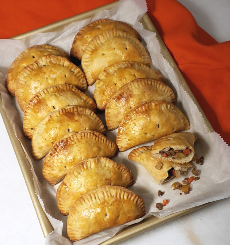Opening Day Michigan Pasties - A baking sheet is lined with these piping hot hand-held meat and vegetable pies. Golden, flaky, half-moon shaped pies are bursting with seasoned ground beef, potatoes, rutabaga, onion and carrots (option for meatless version is provided in the recipe).