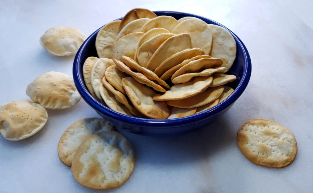 A bowl of these 4-Ingredient Easy Rustic Table Water Crackers are the only thing sitting in the middle of an empty charcuterie board - as if waiting for your suggestions as to which wine and cheese to pair with them.