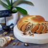 On a round platter sits a loaf of Delicious 3-Step Romanian Colac. Slices of the bread are fanned out to reveal a perfect walnut swirl in the center of the loaf.