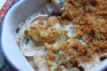 A generous portion of this Perfect Rosemary Gorgonzola Gratin for 2 awaits in a small bowl off to the left of a piping hot casserole dish. Crisp panko and parmesan breadcrumbs top these incredibly creamy gorgonzola scalloped potatoes.