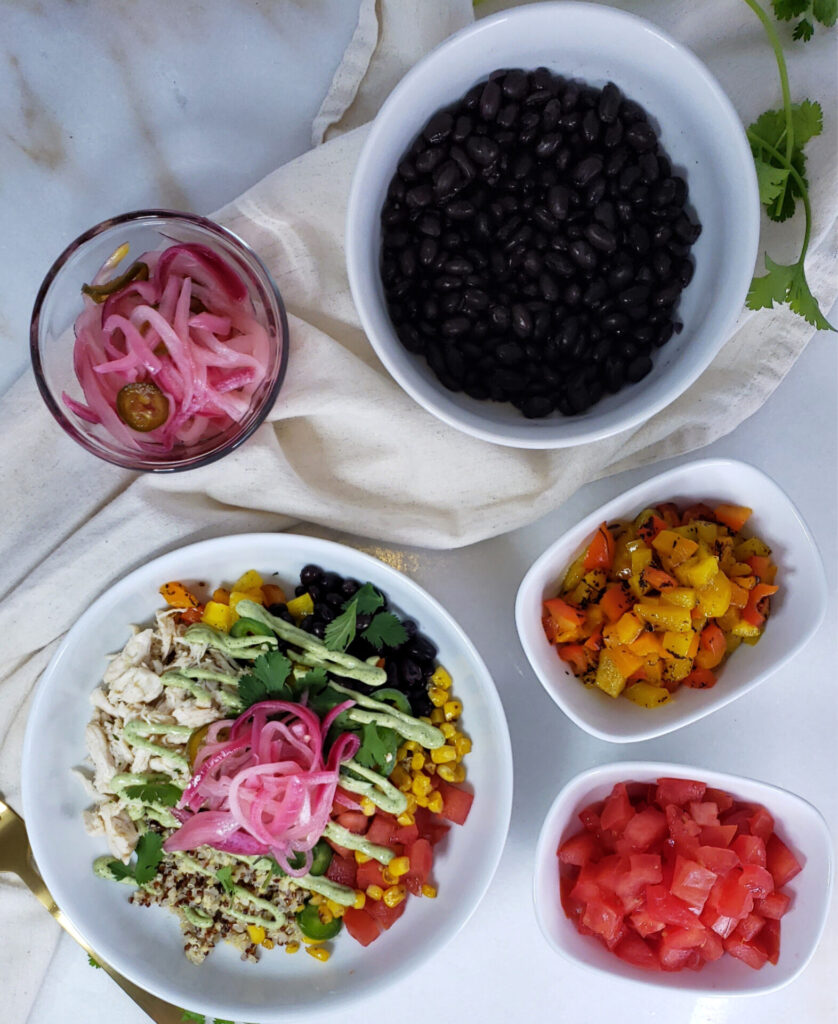 An overhead view of a Healthy 4-Element Power Bowls Buffet. Marinated chicken, black beans, fresh chopped herbs, tomatoes, peppers and corn are neatly arranged on a board. Picked onions and a delicious avocado buttermilk dressing top a beautifully constructed power bowl.