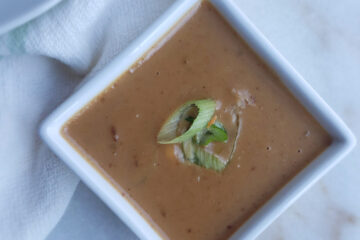 A cup of deliciously creamy Easy 15-minute Thai Peanut Coconut Sauce is topped with fresh, sliced scallions.