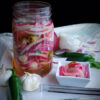 An overhead image of these Quick and Easy Pickled Onions shows a large mason jar full of crisp onions, thinly sliced jalapeno peppers and garlic. The sweet smell of the apple cider vinegar and sugar practically comes through the image.