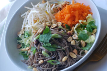 A beautiful bowl of Healthy 4-Element Soba Noodle Salad features fresh napa cabbage, shredded carrots, cilantro, bean sprouts, scallions and peanuts invites you to dig in. A cup of Easy 15-Minute Thai Peanut Coconut Sauce is in the background just waiting to join the salad.