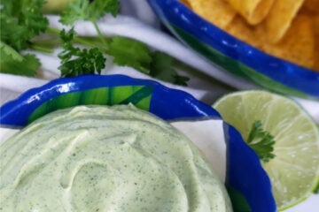 A closeup shot of this Super Simple 5-Minute Avocado Buttermilk Dressing. This dressing looks so light and flavorful with its creamy texture and fresh herbs. In the background is a bowl of crisp tortilla chips, more fresh herbs, and avocado and lime that have been cut in half. They are at their peak freshness.