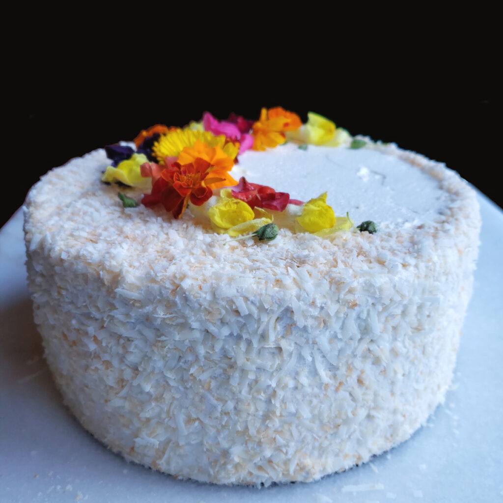 Fresh edible flowers and lightly toasted coconut adorn this Easy Pineapple Coconut Cake with 5-Ingredient Rum Buttercream.