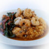 A bowl of cheese grits with a side of greens is topped off with a tower of Easy Spicy Cajun Shrimp in 30 MInutes. Soak up this flavorful sauce with a chunk of french bread.