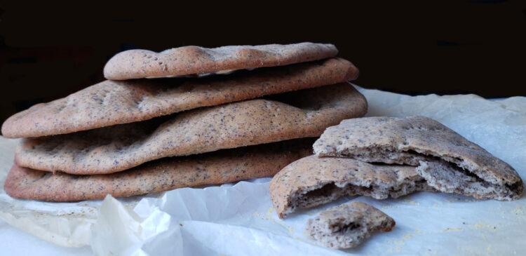 A beautiful stack of fresh bakes Easy 7-Ingredient Rustic Buckwheat Flatbreads rest upon a sheet of parchment paper. One of the flatbreads is torn in half to reveal its light texture inside.