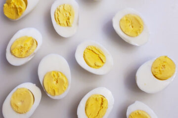 A cutting board displays perfectly cooked hard boiled eggs that have been sliced in half. The yolks are vibrant yellow - without the unappealing dark green ring that can form around them when eggs are cooked too long or at too high a temperature.