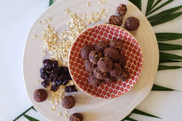 A plate of 7-Ingredient No Bake Energy Bites are stacked in a perfect pyramid. Oats and dried cherries are strewn across the wood cutting board on which the plate sits.