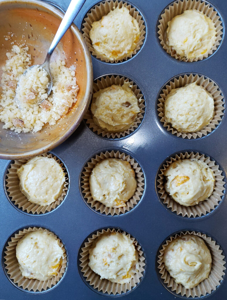A muffin tray full of Bold Ginger Mango Muffins with Sesame Streusel wait to be baked.