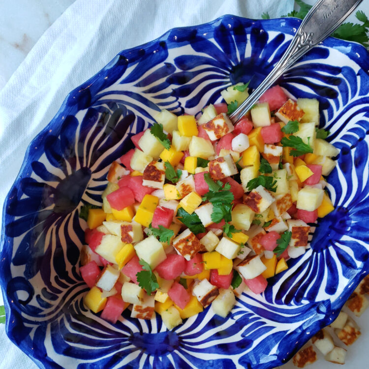 A large Mexican-style bowl is filled with Fresh and Easy 4-Fruit Salad with Warm Cheese. Crisp jicama, fresh pineapple, watermelon and mango are lightly dressed in lime juice and agave nectar and finished with cubes of warm Halloumi-style cheese that has been grilled and fresh cilantro or mint.