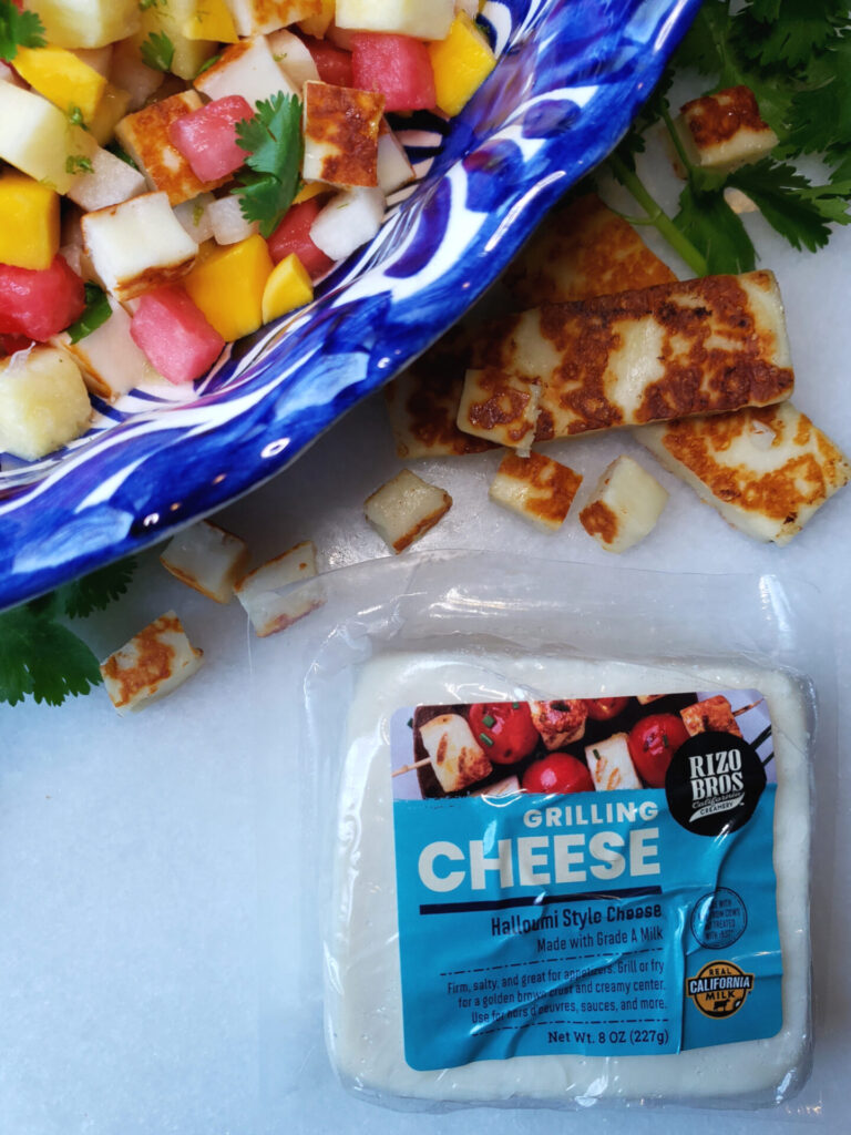 A large Mexican-style bowl is filled with Fresh and Easy 4-Fruit Salad with Warm Cheese. Crisp jicama, fresh pineapple, watermelon and mango are lightly dressed in lime juice and agave nectar and finished with cubes of warm Halloumi-style cheese that has been grilled and fresh cilantro or mint.