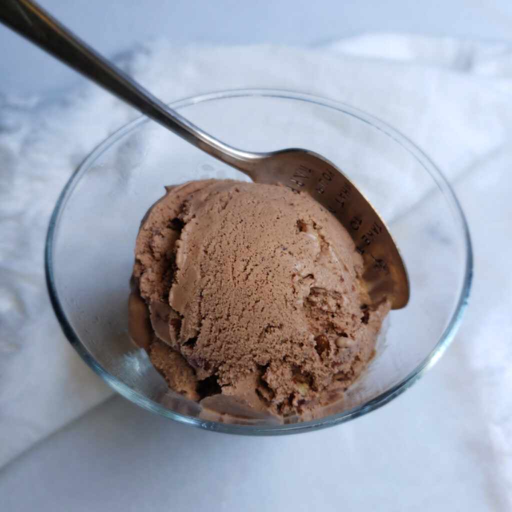 A cool and refreshing scoop of Easy 7-Ingredient Mexican Chocolate Ice Cream is nested in an ice cream scoop. Disks of Mexican Chocolate and toasted almonds are in the background.
