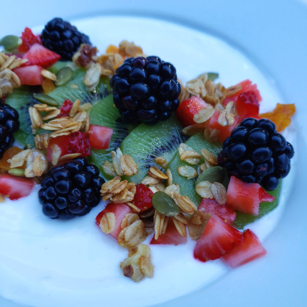 A bowl of greek yogurt is topped with fresh kiwi, blackberries and strawberries and topped with a generous sprinkling of Crazy Simple 15 Minute Skillet Granola