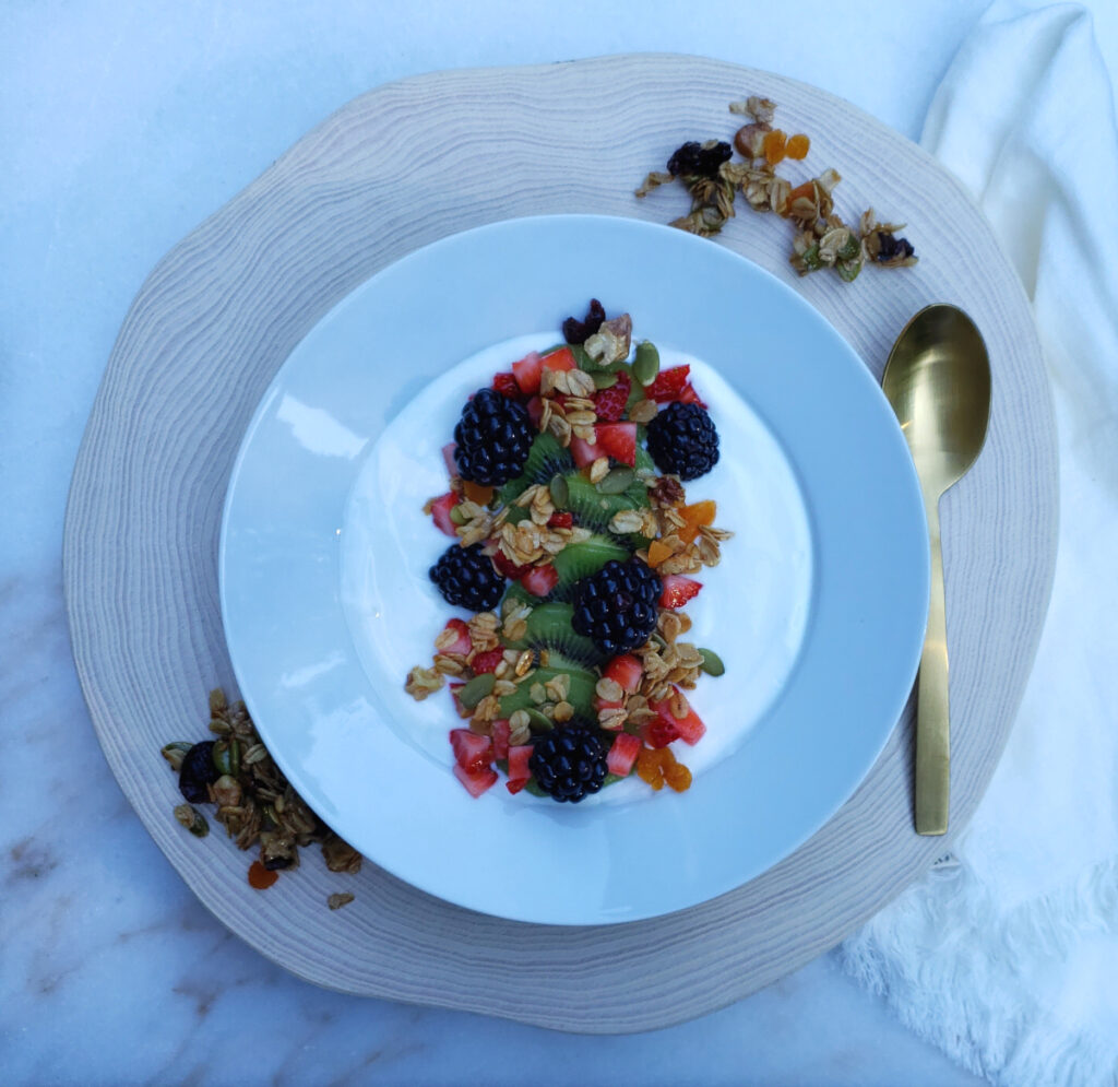 A bowl of greek yogurt is topped with fresh kiwi, blackberries and strawberries and topped with a generous sprinkling of Crazy Simple 15 Minute Skillet Granola