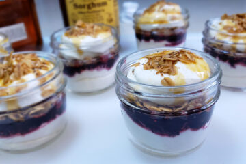 Glass jars of Appalachian Cranachan in 3 Easy Steps feature layers of bourbon and honey-infused whipped cream, fresh berries and toasted honey oats.