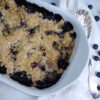 Hot out of the oven, a baking dish of bubbly hot Amazing Honolulu Blueberry Crisp in 90 Minutes sits cooling on a white marble countertop.