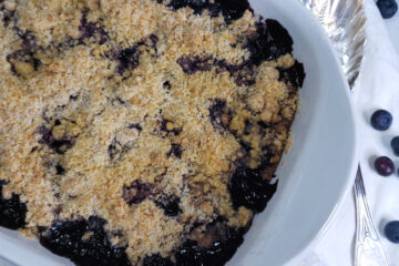 Hot out of the oven, a baking dish of bubbly hot Amazing Honolulu Blueberry Crisp in 90 Minutes sits cooling on a white marble countertop.