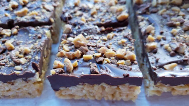 A closeup shot of these delicious and Easy Tahini Toffee Crispy Rice Bars in 15 Minutes. A layer of tahini-flavored rice treats is topped with a thin layer of dark chocolate and a sprinkling of English toffee bits.