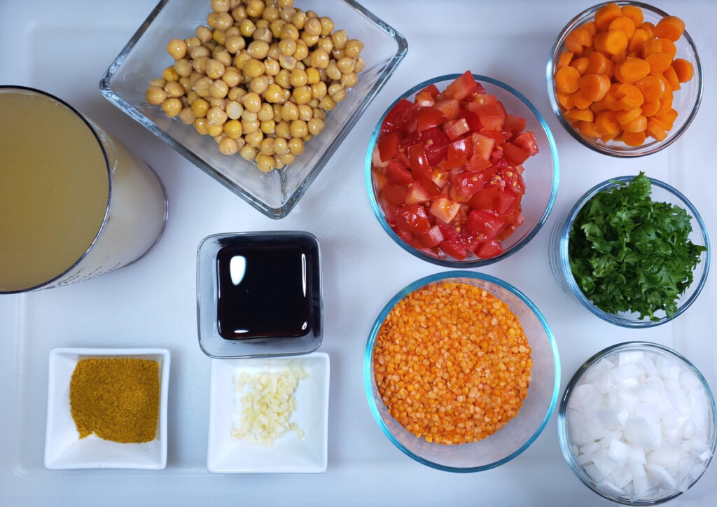 All the ingredients for this Easy Vegetarian Curried Lentil Soup in 1 Hour are cut up and neatly arranged on a cutting board. Vegetable or chicken stock, chick peas, diced tomatoes, diced carrots, fresh parsley, white onion, red lentils, red wine, garlic, yellow curry powder and salt and pepper.