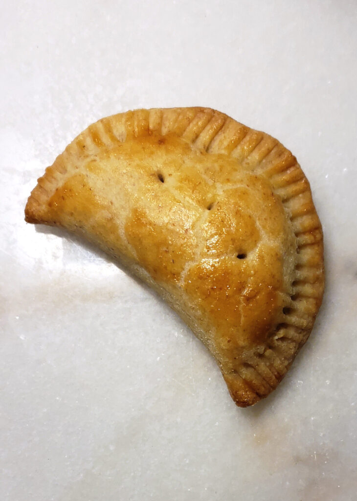 A perfectly shaped half-moon Easy Opening Day Michigan Pasties. The crust is glazed with an egg wash and is a rich golden brown.