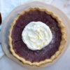 A serving platter and elegant golden pie knife frame this Stunning 8-Ingredient Purple Sweet Potato Pie reveals a vibrant purple color, and creamy texture. Topped with fresh whipped cream and lemon zest.