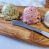 A flight of Easy Sweet and Savory Compound Butter 4 Ways sits upona serving board. From right to left, a scoop of Rum Raisin, Spiced Orange Cranberry, Lemon Dill and Garlic Herb compound butters sit ready. No more boring roll and butter.