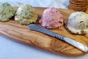 A flight of Easy Sweet and Savory Compound Butter 4 Ways sits upona serving board. From right to left, a scoop of Rum Raisin, Spiced Orange Cranberry, Lemon Dill and Garlic Herb compound butters sit ready. No more boring roll and butter.