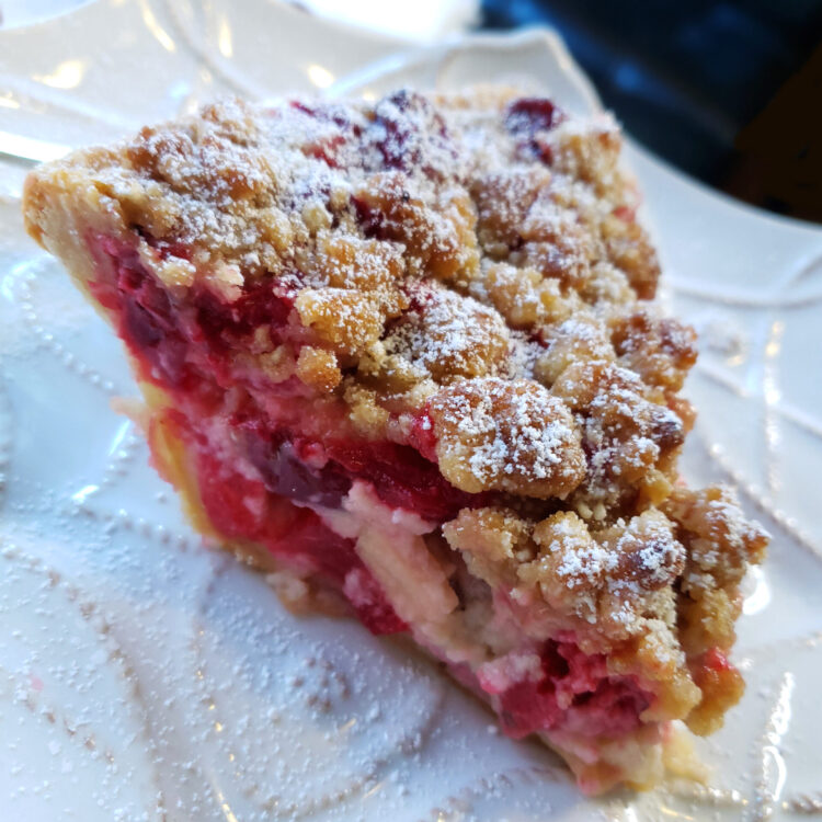 A closeup of a slice of this Easy as 1-2-3 Cranberry Custard Pie shows a beautifully flaky crust. Fresh cranberries are suspended in a simple custard and topped with a delicious crumb topping. The pie is lightly dusted with powdered sugar for an elegant effect.
